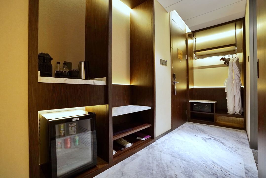 Habitación de hotel con minibar, espejo, repisa con artículos de tocador y bata colgada en un perchero.