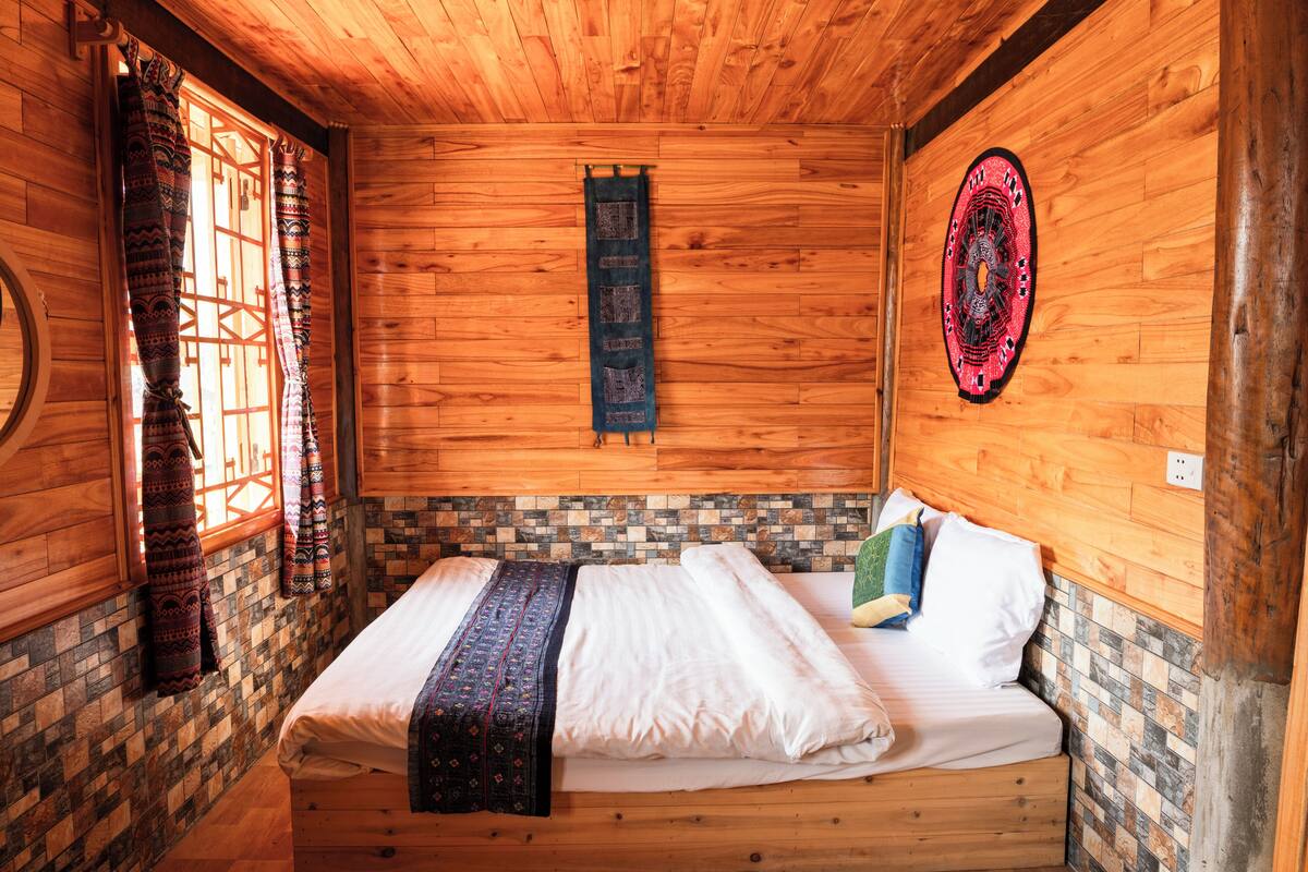 A wooden room with a bed, patterned curtains, a wall clock, and a decorative wall piece.