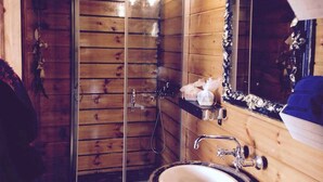 A wooden cabin bathroom with a glass shower enclosure, a sink with a mirror, and a shelf with toiletries. - Ambelli The Pirates Cabin - Black Pearl (Kalymnos)