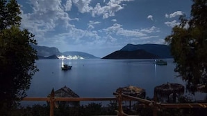A calm lake with a boat, a thatched-roof hut, and a wooden fence. - Ambelli The Pirates Cabin - Black Pearl (Kalymnos)