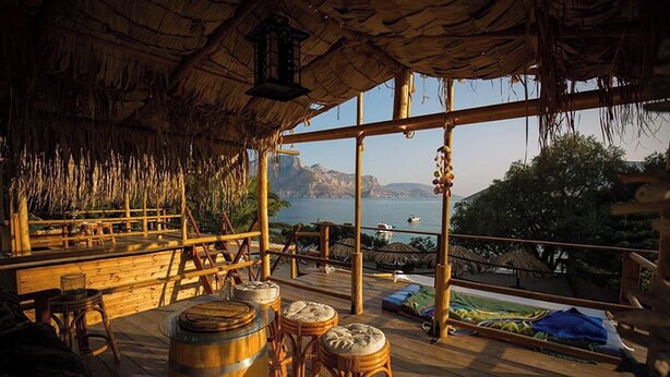 A wooden deck with a thatched roof, wooden furniture, and a view of the sea. - Ambelli The Pirates Cabin - Black Pearl (Kalymnos)