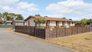 Une rangée de chalets de plain-pied, avec une clôture en bois à l’avant, une allée pavée et une zone herbeuse.