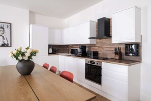 Une cuisine moderne avec des meubles blancs, un plan de travail en bois, une machine à café noire et un vase de fleurs blanches posé sur la table.