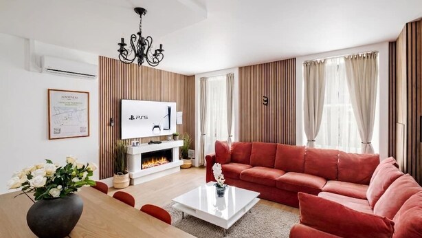 A modern living room with a fireplace, a red sofa, a white coffee table, and a chandelier. - Stunning 2BR 2BA in the ♥️ of Marylebone ❄️ Air Conditioning | Sleeps 8 (Greater London)