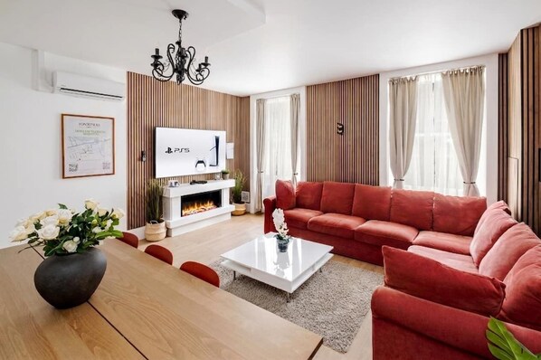 Un salon moderne avec une cheminée, un canapé rouge, une table basse blanche et un lustre.