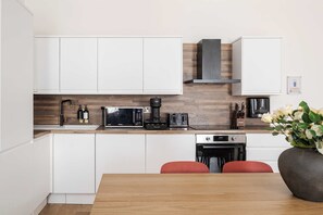 A modern kitchen with white cabinets, a microwave, a coffee maker, and a toaster. There is a wooden countertop and a vase with flowers on the table.