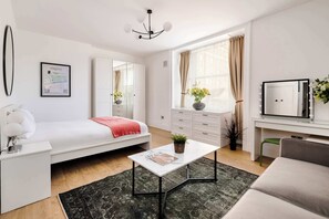 Une chambre à coucher moderne avec un lit, un bureau blanc, un miroir, une commode et une fenêtre avec des rideaux.