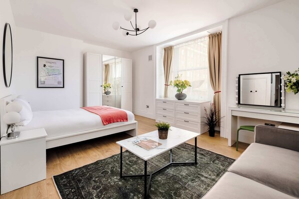 A modern bedroom with a bed, a white desk, a mirror, a dresser, and a window with curtains.