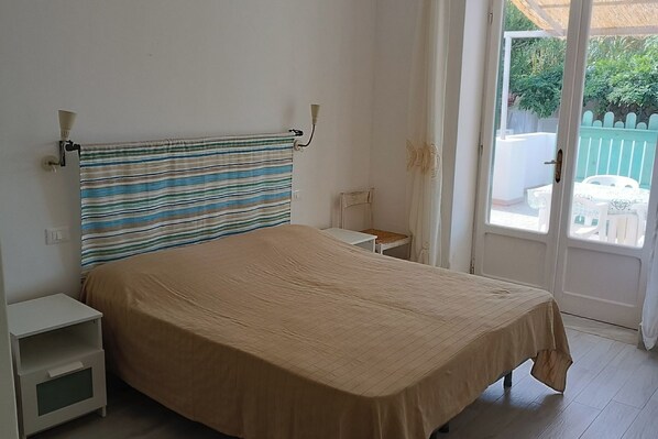 A bedroom with a bed, a nightstand, a chair, and a view of the outside.