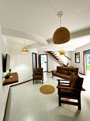 A spacious living area with a sofa set, a chair, a TV, and a staircase leading to another level.