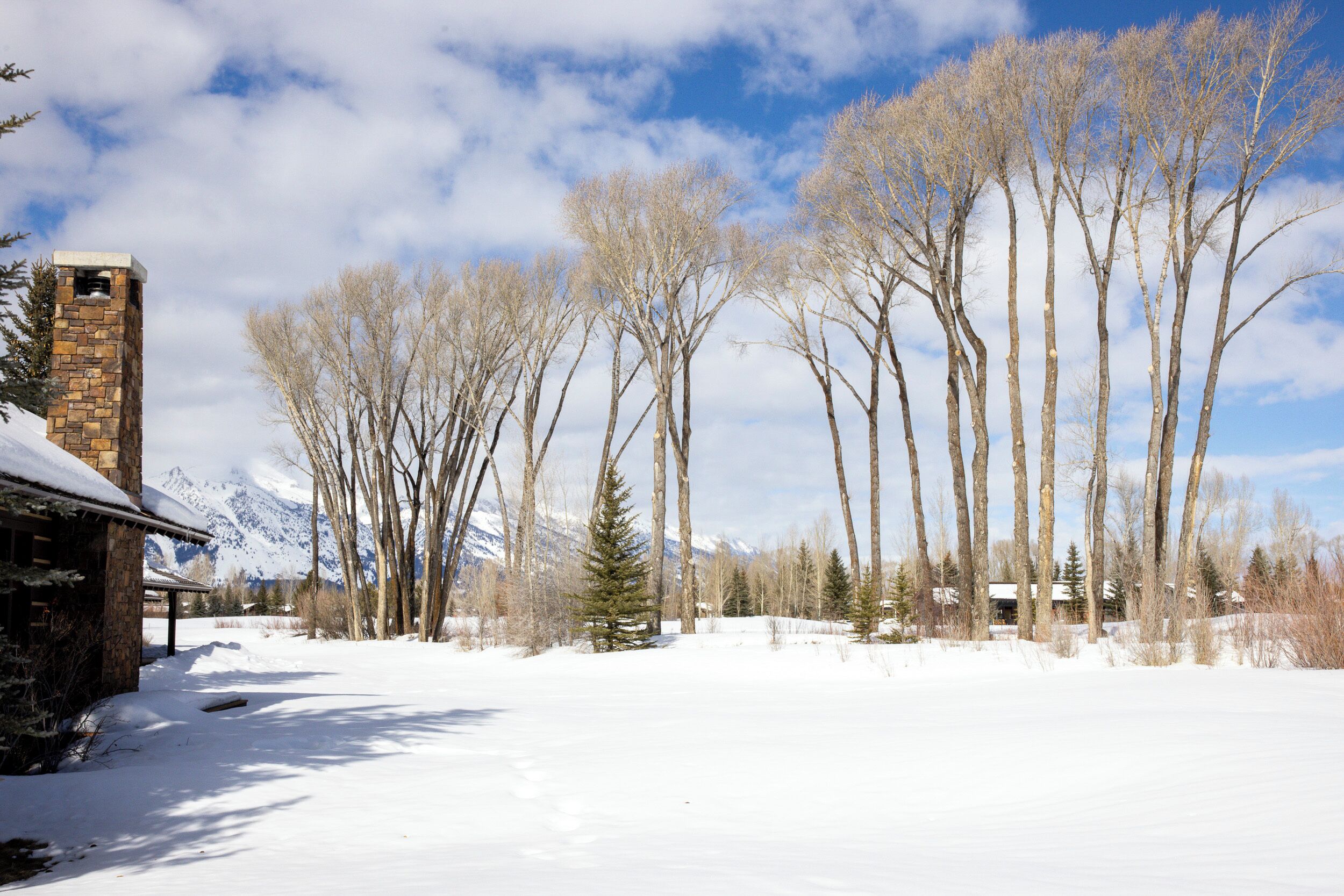 Un paysage enneigé avec un bâtiment en pierre, des arbres sans feuilles et des montagnes en arrière-plan.