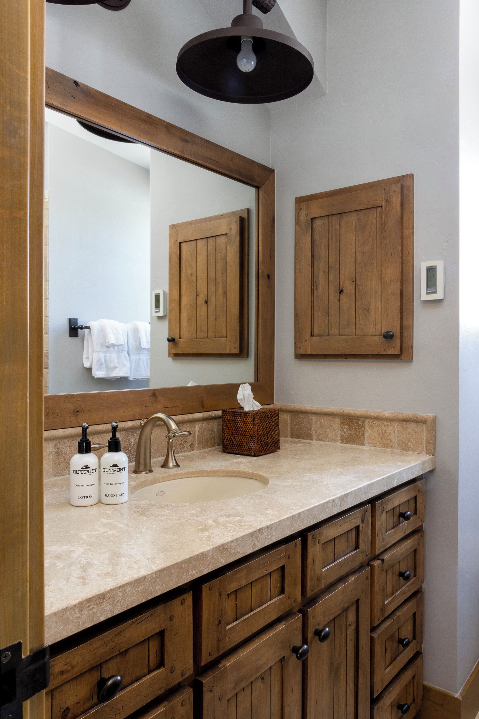 A bathroom with a large mirror, wooden cabinets, a sink, and two bottles of Outpost hand soap.
