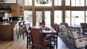 Un comedor amplio con una mesa y sillas de madera, una araña y ventanas grandes que ofrecen vistas al exterior.