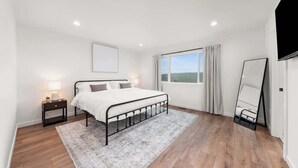 A bedroom with a bed, bedside tables, a window with curtains, and a mirror. - River Ridge Villa- New Build! (Spokane)