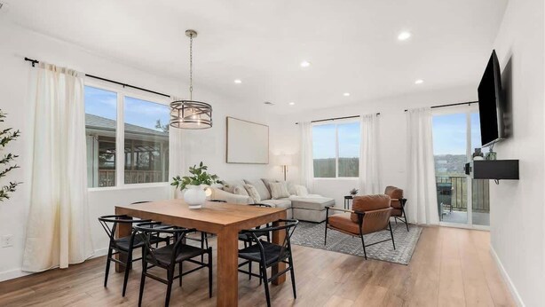A modern living room with a wooden dining table, black chairs, a sofa, and a TV mounted on the wall. - River Ridge Villa- New Build! (Spokane)