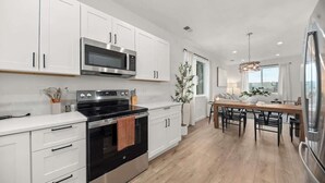 A modern kitchen with white cabinets, stainless steel appliances, and a wooden dining table with chairs. - River Ridge Villa- New Build! (Spokane)