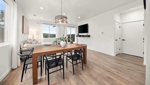 A modern kitchen with a wooden dining table, black chairs, and a hanging light fixture. - River Ridge Villa- New Build! (Spokane)