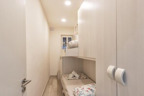 Un couloir étroit mène à une pièce où se trouve un lit superposé, une porte avec un trou de serrure et un porte-rouleau de papier toilette fixé au mur.