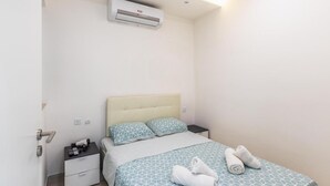 A hotel room with a bed, bedside tables, an air conditioning unit, and a towel on the bed. - Seafront Designer Bliss in Central St Julian's (St. Julian's)