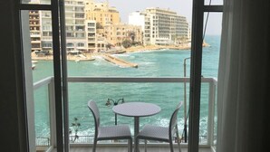 A balcony with two chairs and a small table, overlooking a coastal area with buildings and a beach. - Seafront Designer Bliss in Central St Julian's (St. Julian's)