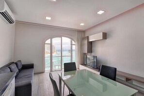 Une chambre d’hôtel moderne avec une table à manger en verre, un canapé, une télévision et une vue sur l’océan.