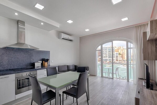 A modern kitchen with a dining area, a large window with a view of the city, and a built-in oven. - Seafront Designer Bliss in Central St Julian's (St. Julian's)