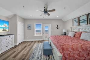 A bedroom with a bed, a ceiling fan, a dresser, a bench, a rug, and a door leading to a balcony.