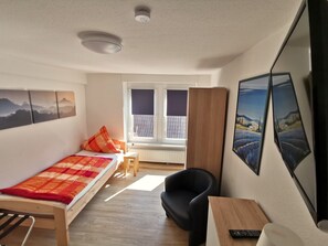 A bedroom with a bed, a desk, a chair, and a window with blinds. - Hotel-Pension zum Hirsch (Hattersheim)
