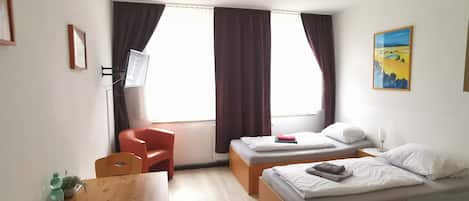 A hotel room with a bed, a desk, a chair, a TV, and a window with curtains.