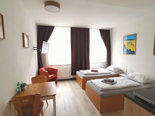 A hotel room with a bed, a desk, a chair, a TV, and a window with curtains. - Hotel-Pension zum Hirsch (Hattersheim)