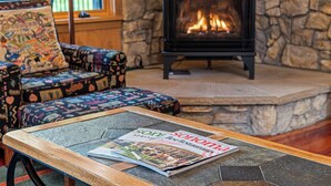 Un salón acogedor con chimenea de piedra, un sillón estampado y una mesa con una revista.
