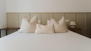 Ein ordentlich bezogenes Bett mit vier Kissen, ein Nachttisch mit Lampe und eine Wandverkleidung.