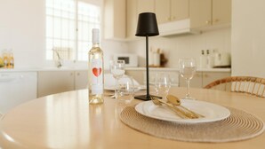 Ein Esszimmertisch ist gedeckt mit einer Weinflasche, Gläsern und Besteck in einer hellen Küche mit weißen Schränken und einem Fenster.