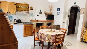 A kitchen with wooden cabinets, a gas stove, a coffee maker, and a dining area with a table set for two. - Casa rita - beach house with garden and bbq grill (Sant'Andrea Apostolo Dello Ionio Marina)