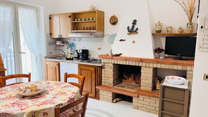 A kitchen with wooden cabinets, a built-in stove, and a dining area with a table set for two. - Casa rita - beach house with garden and bbq grill (Sant'Andrea Apostolo Dello Ionio Marina)