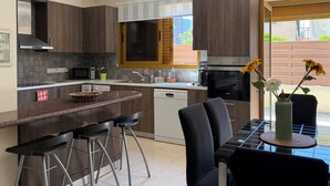 Una cocina moderna con armarios de madera oscura, un microondas empotrado, un horno de acero inoxidable y un comedor con mesa de vidrio y sillas negras.
