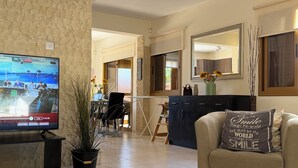 Una sala de estar moderna con una televisión, un sofá con un cojín motivacional, un cuenco negro y una planta en maceta.