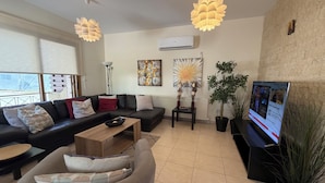Una sala de estar moderna con sofá, mesa de centro, televisor y plantas decorativas.