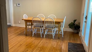 A dining area with a wooden table and four white chairs, a chandelier, and a potted plant.
