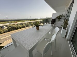 Ein Balkon mit einem weißen Tisch und Stühlen, einem Blumentopf und Blick auf eine Autobahn und Gebäude.