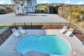 A swimming pool with lounge chairs, a fenced deck, and a building in the background. - Perfect 8BR Beach Getaway: Pool, Hot Tub, Ocean Views (North Topsail Beach)