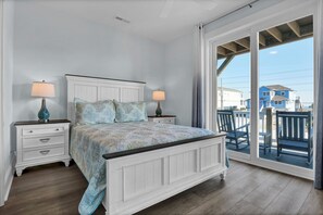A bedroom with a bed, two nightstands, a dresser, and a large sliding glass door leading to a balcony. - Perfect 8BR Beach Getaway: Pool, Hot Tub, Ocean Views (North Topsail Beach)