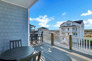 A wooden deck with a table and chairs, overlooking a beach with houses in the background. - Perfect 8BR Beach Getaway: Pool, Hot Tub, Ocean Views (North Topsail Beach)