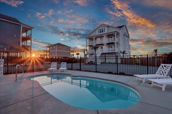 A swimming pool with lounge chairs, a fence, and a building with multiple balconies. - Perfect 8BR Beach Getaway: Pool, Hot Tub, Ocean Views (North Topsail Beach)