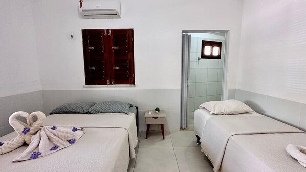 Une chambre d’hôtel avec deux lits, une petite table de chevet, un climatiseur fixé au mur et une porte donnant sur une autre pièce.