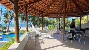 Un espacio al aire libre techado con piscina, sillas, una hamaca y una parrilla.