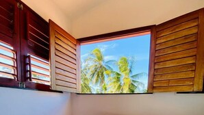 Una cama con vistas a palmeras a través de contraventanas de madera.