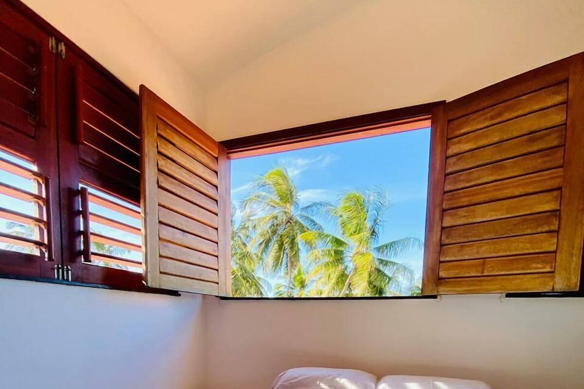 Cama com vista para palmeiras através de persianas de madeira.