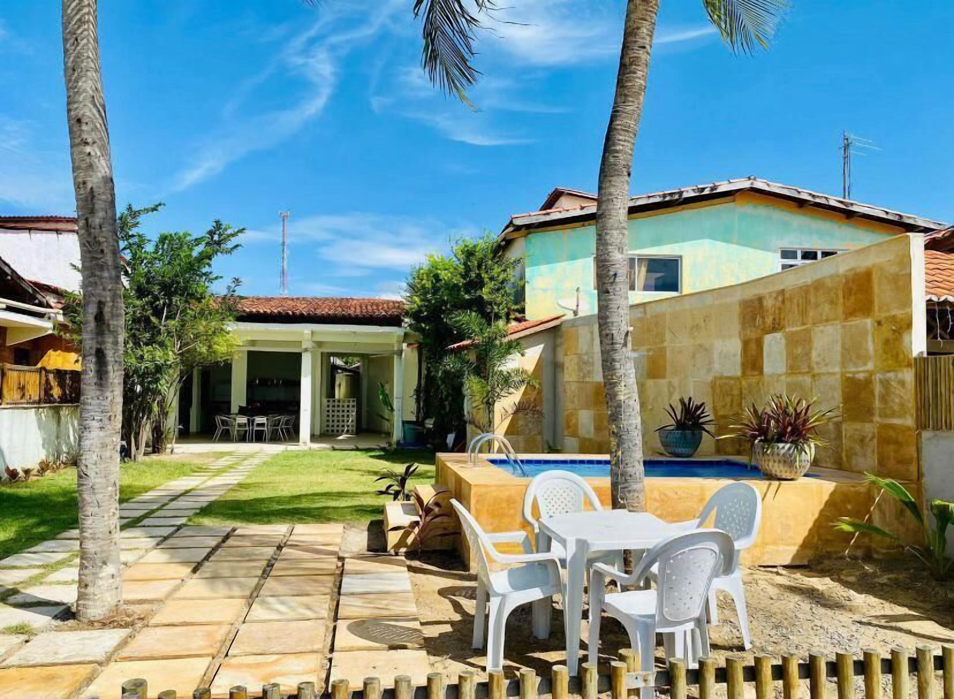 A patio with a pool, white plastic chairs, and a small table.