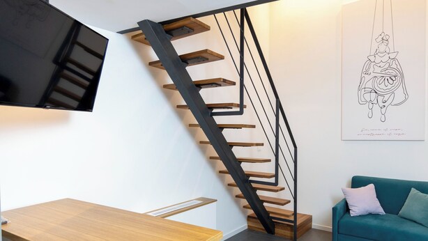 Un interior moderno con una escalera de madera, un sofá color esmeralda y una obra de arte colgada en la pared.
